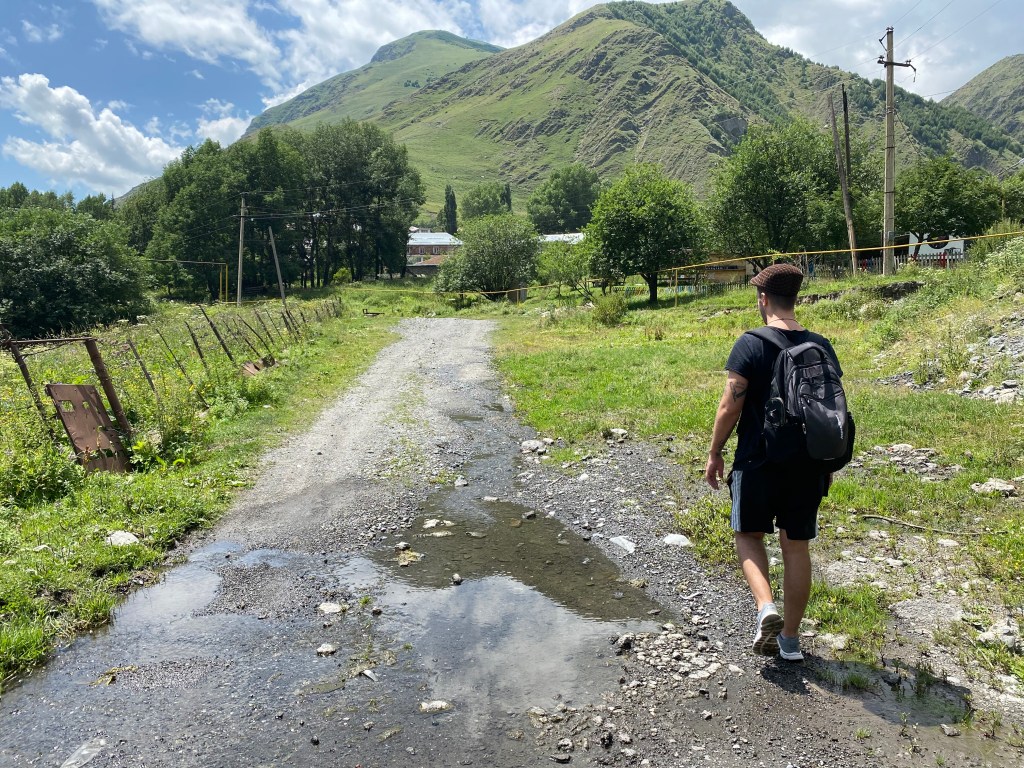 A man walks down a dirt path in the countryside of Georgia. Kazbegi, Stepantsaminda.