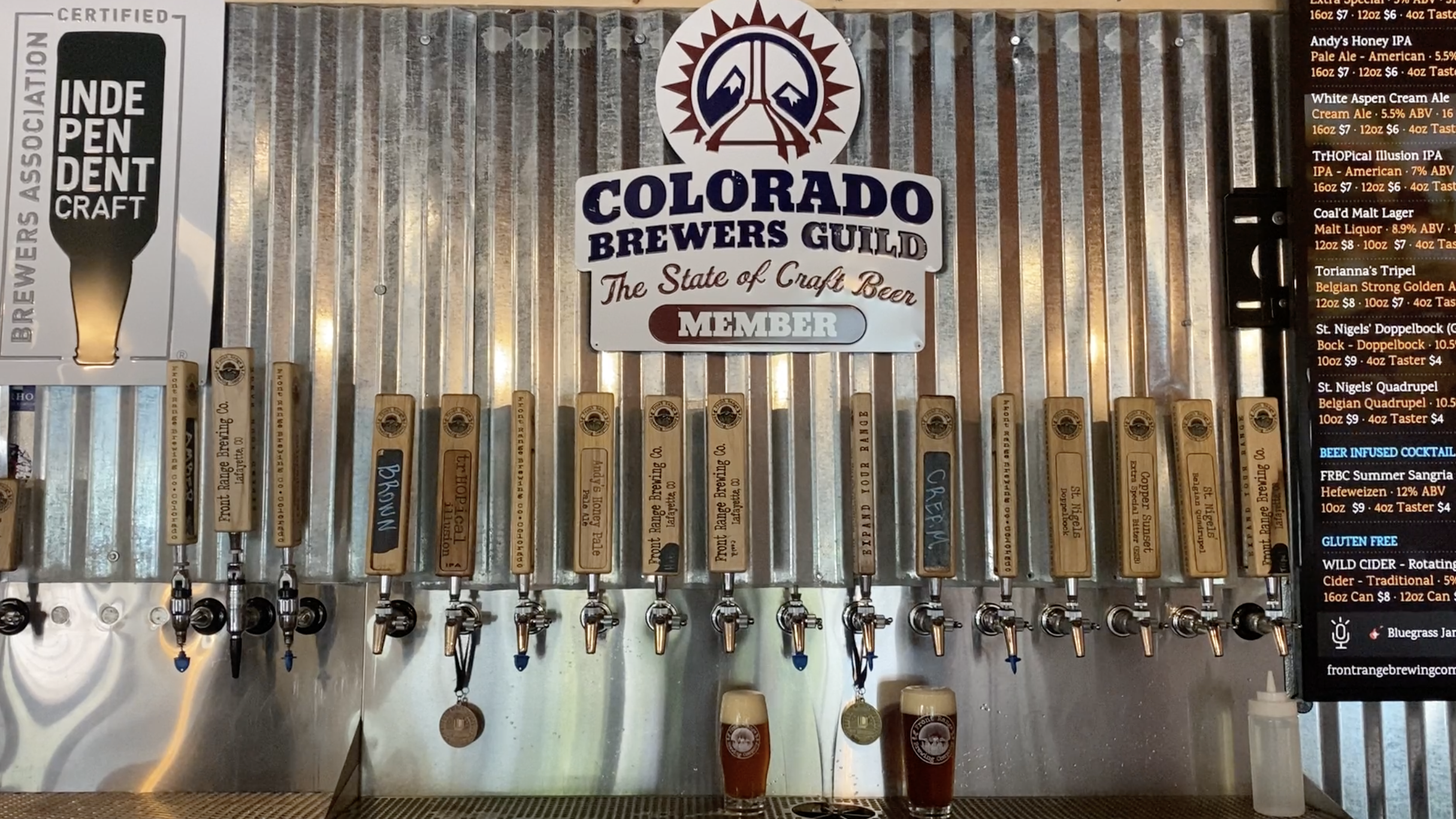 Lafayette Colorado Brewery: This is a photo of a bar with several beer taps on the silver wall of corrugated metal. Above the taps is a sign that says "Colorado Brewer's Guild."