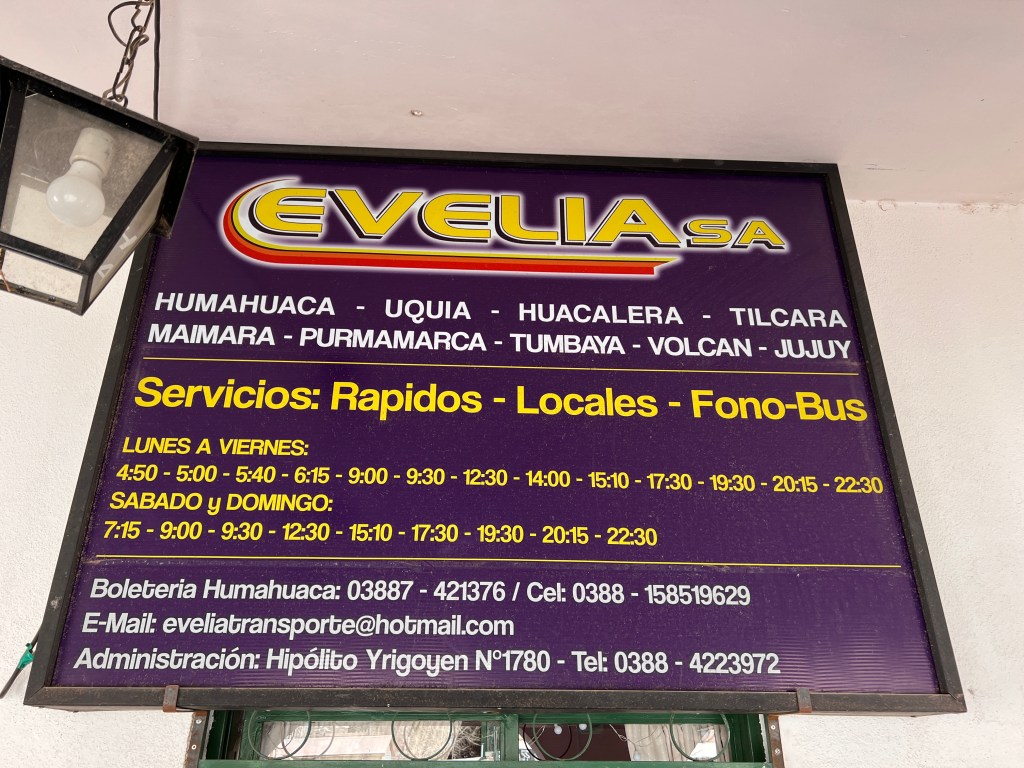 This is a purple sign with yellow writing. It shows the bus schedule with the Evelia bus company from Humahuaca to several other towns.