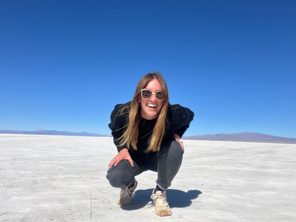 Nicki kneels down on the salt flats at the salinas grandes in jujuy, argentina. She explains how to keep your US phone number while abroad.