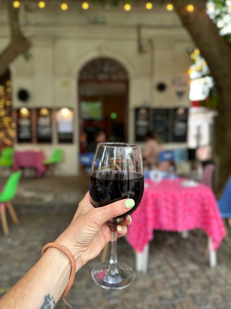 Nicki holds out a glass of red wine in front of Que Tupe, a cute restaurant in Colonia del Sacramento