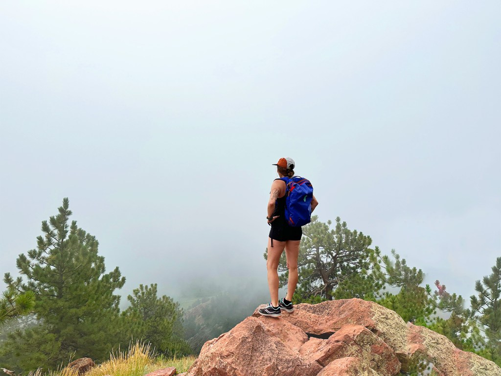 Mount Sanitas Trail: Nicki stands on top of a rock at the peak of Mount Sanitas Trail. She looks out into the distance but there is a lot of fog.