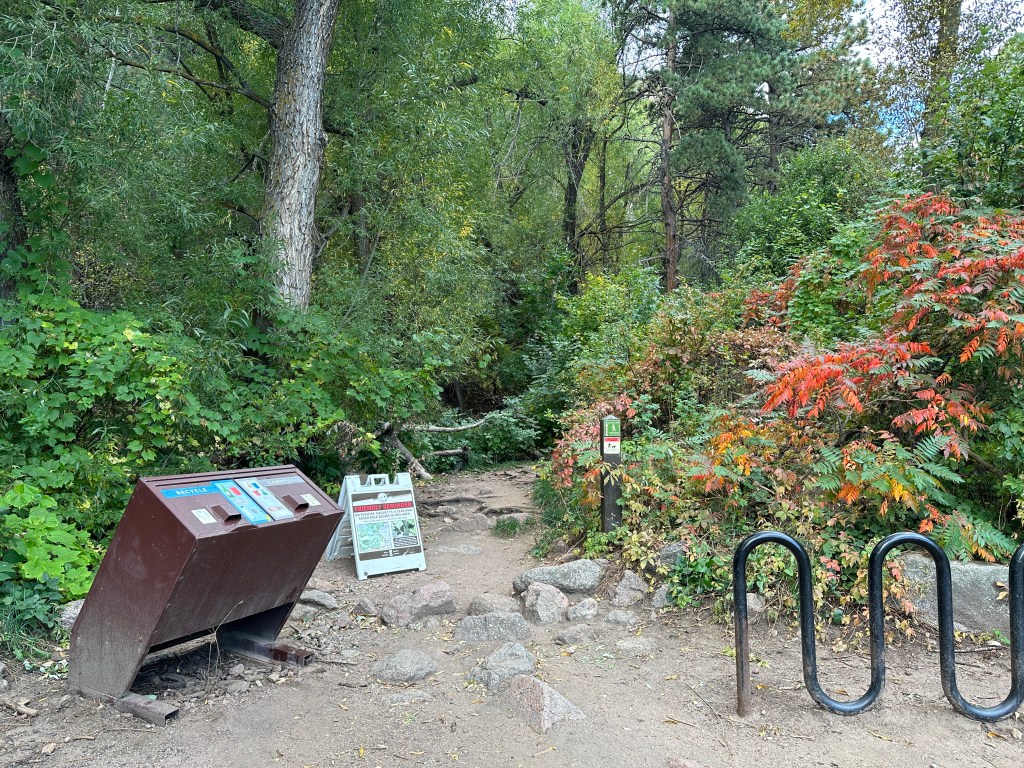 There are two trash cans and a bike rack next to the start of the Gregory Canyon to Flagstaff Mountain Path.