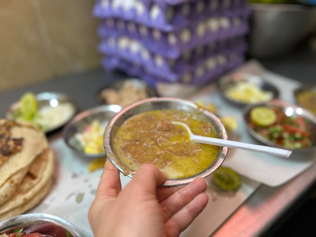 This is a hand holding a bowl of fuul. It is fava beans in a silver dish.