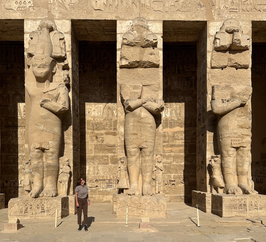 know before going to egypt: you can't do all the things, you have to choose. This is a photo of Nicki looking very small next to giant statues at the temple of Habu.