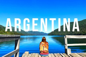 a blue lake and a blue sky. Nicki sits on the edge of a dock. The word on top says ARGENTINA