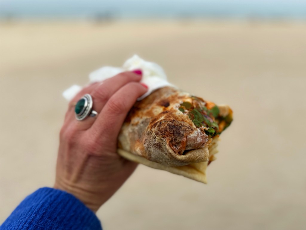 Things to do in Sousse: eat local food. This is a hand holding a mlawi in front of the beach.