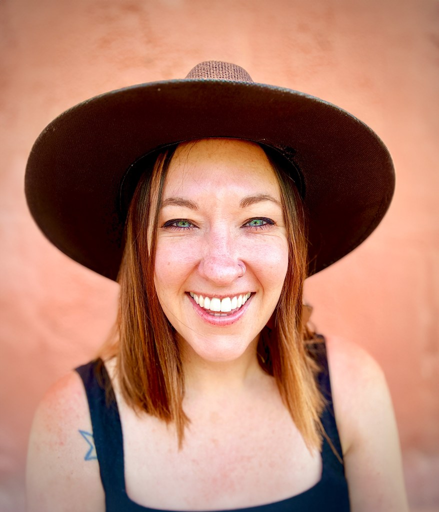A photo of Nicki in front of an orange wall wearing a black hat in Mexico.