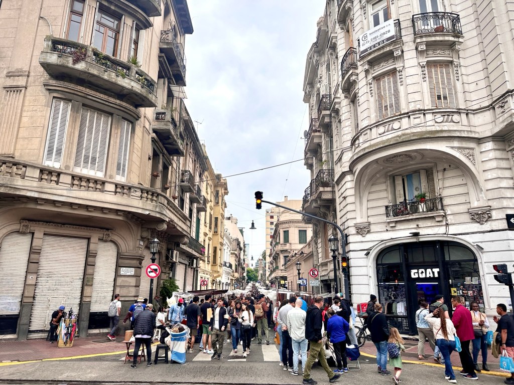 It's a busy day with many people walking around the cobblestone streets of the San Telmo Market on a Sunday in Buenos Aires.