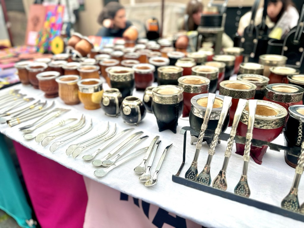 Several mate cups and metal straws (bombillas) are on a table for sale at the San Telmo Market in Buenos Aires.