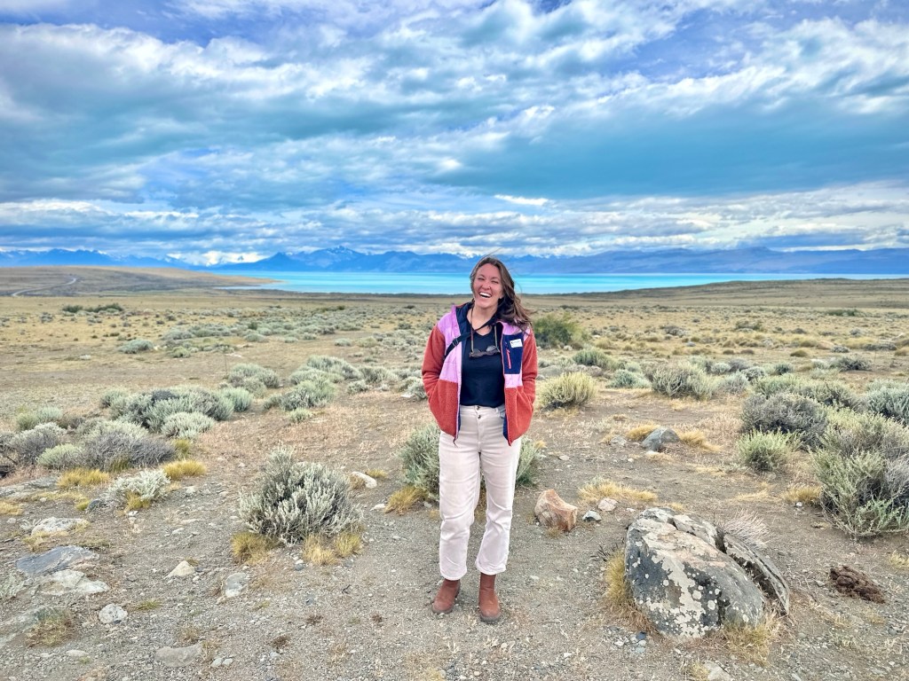 Nicki stands in a field in front of Lago Argentino next to the Glaciarium Museum.