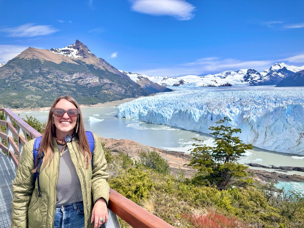 Nicki wears jeans and a green Levis jacket, and smiles at the camera. Behind her is the famous Perito Moreno glacier outside of El Calafate Argentina.