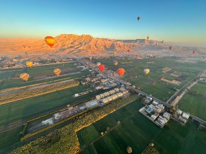 This is a birds eye view of Luxor from a hot air balloon. You can see the green fields below with the mountains in the distance. You can see the sun reflecting on the mountains for sunrise.
