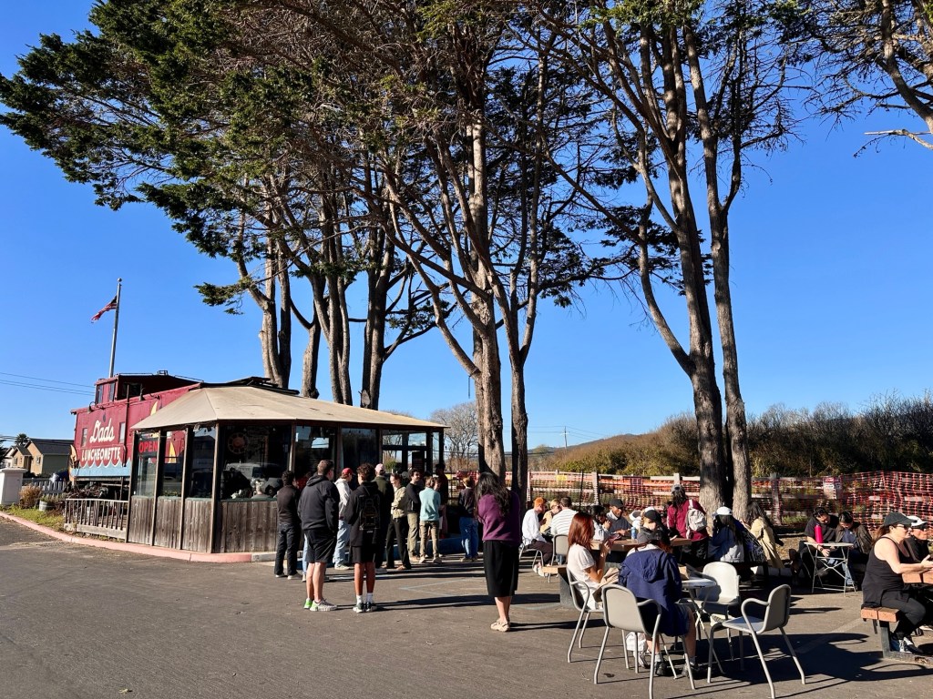 A crowd stands outside of Dad's Luncheonette waiting for food.